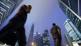 Pedestrians walk past commercial buildings including the Shanghai Tower, center left, as it stands under construction at night in the Lujiazui district of Shanghai, China, on Friday, June 28, 2013. China's President Xi Jinping said officials shouldn't be judged solely on their record in boosting gross domestic product, the latest signal that policy makers are prepared to tolerate slower economic expansion. Photographer: Tomohiro Ohsumi/Bloomberg