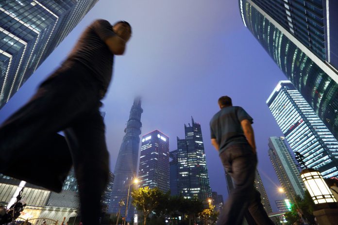 Pedestrians walk past commercial buildings including the Shanghai Tower, center left, as it stands under construction at night in the Lujiazui district of Shanghai, China, on Friday, June 28, 2013. China's President Xi Jinping said officials shouldn't be judged solely on their record in boosting gross domestic product, the latest signal that policy makers are prepared to tolerate slower economic expansion. Photographer: Tomohiro Ohsumi/Bloomberg